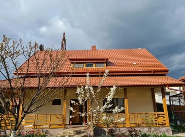Casă cu acoperiș din țiglă ceramică roșie și terasă din lemn